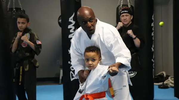 An Urban Spirit Foundation instructor guiding a young student in a white gi through a stance as other students train behind them